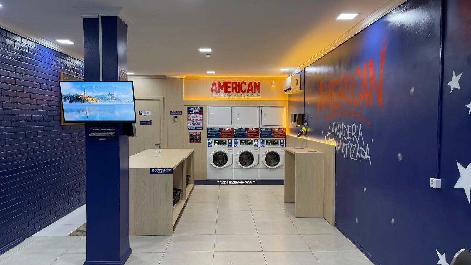 Salão com parede azul, bancadas de dobra e máquinas ao fundo